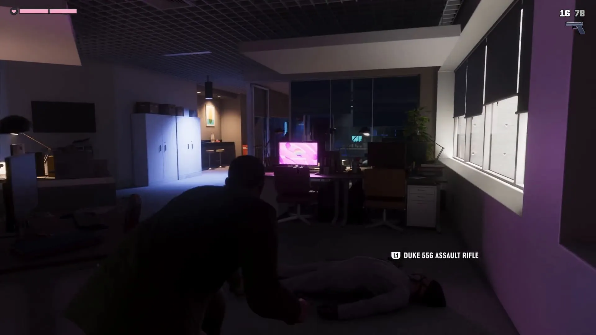 An Extended Look frame: Jason crouches in a dark office in the Megamundo tower next to a downed man, and the Duke 556 Assault Rifle pickup prompt appears on screen