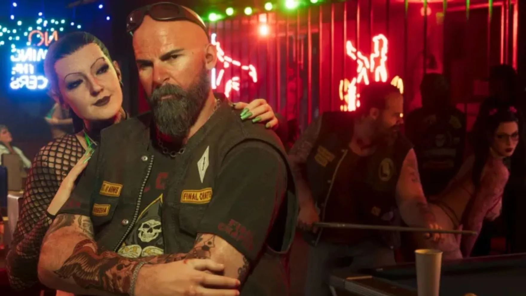 Official GTA VI screenshot: a bearded biker in a leather vest with a woman's arms around him in a red neon-lit bar, with other bikers around the pool table