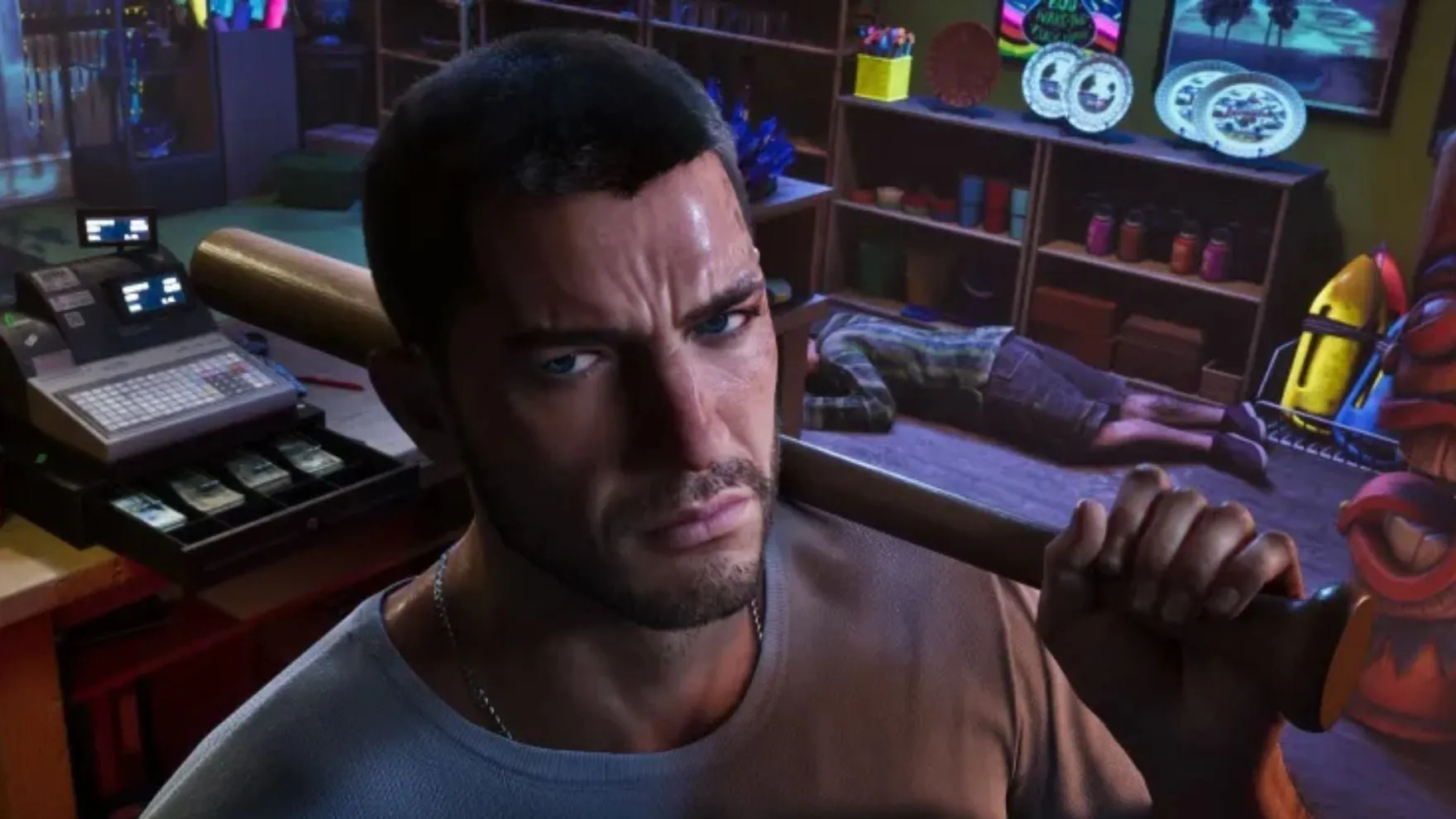 Screenshot ufficiale di GTA VI: Jason con una mazza da baseball in spalla in un negozio di souvenir, accanto a un registratore di cassa col cassetto aperto pieno di banconote e il commesso a terra