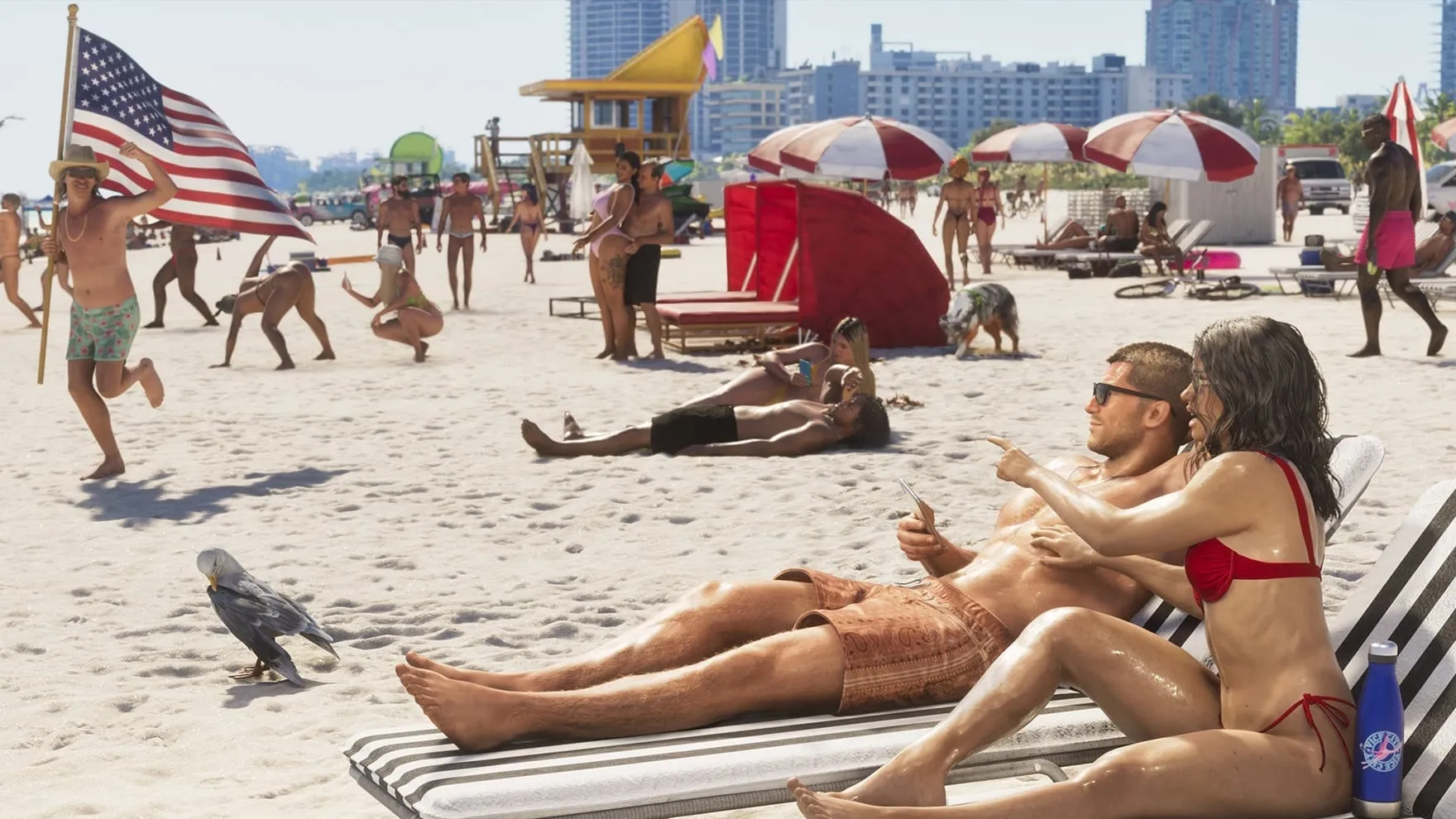 Screenshot ufficiale di GTA VI: Jason e Lucia sdraiati sui lettini di una spiaggia affollata di Vice City, lei indica qualcosa, mentre un uomo corre dietro di loro con una bandiera americana