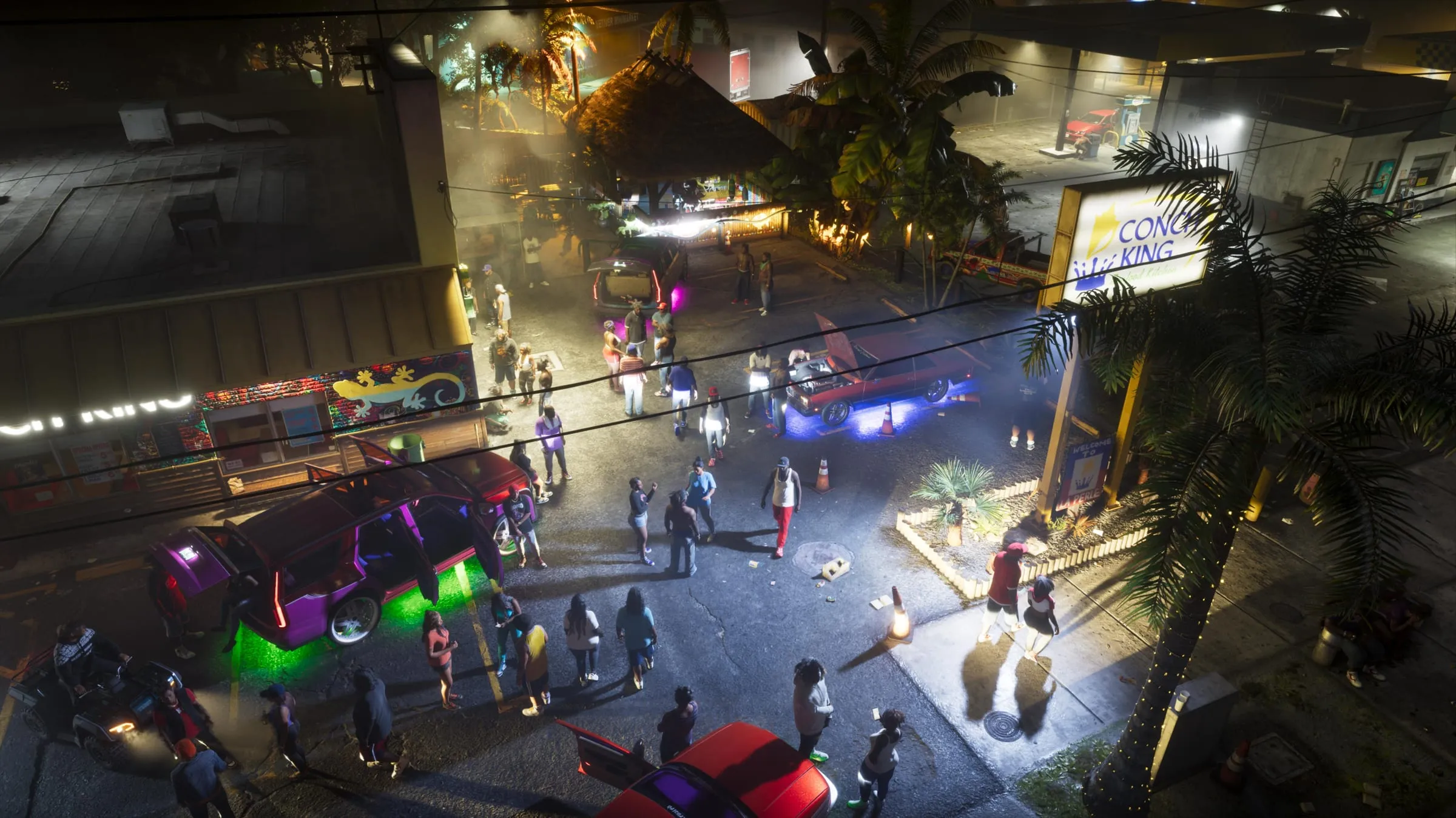 A night car meet seen from above, with a green-underglow SUV, a red lowrider with its hood up and a crowd by the Conch King sign