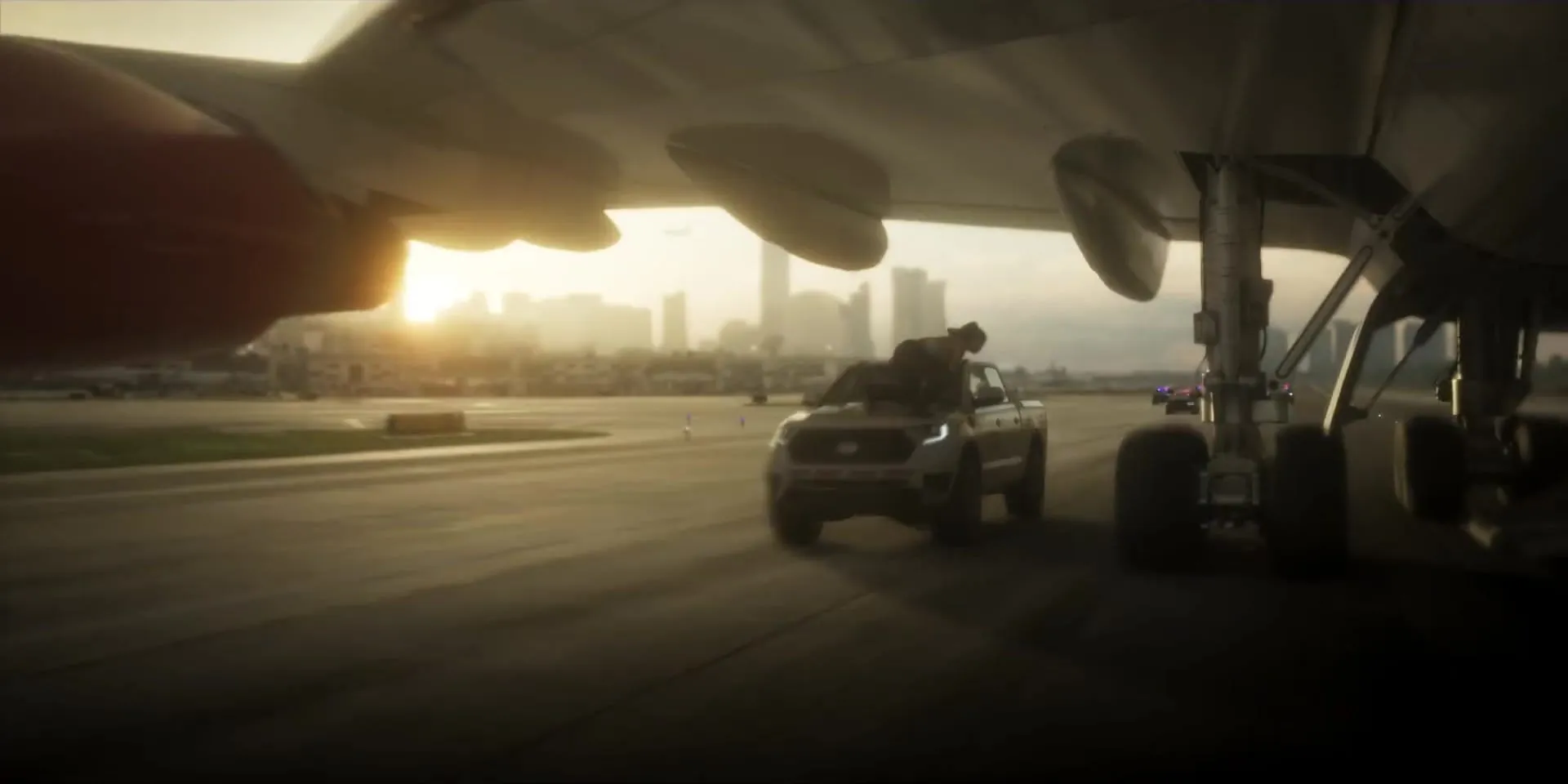 A pickup on an airport runway under an airliner wing, with the skyline at sunset
