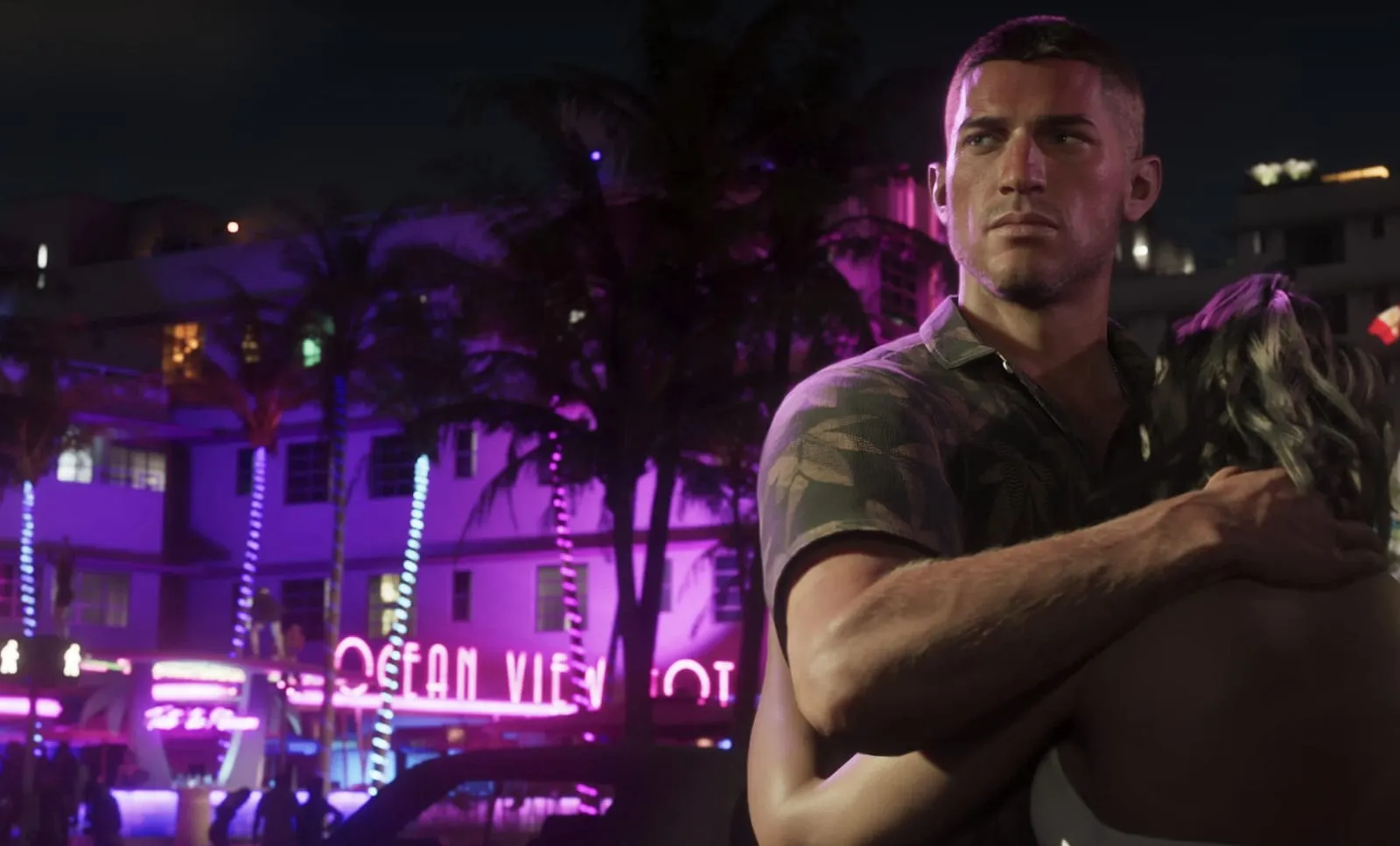 Fotogramma ufficiale di GTA 6: Jason di notte su Shore Drive, alle sue spalle la facciata dell'Ocean View Hotel con l'insegna al neon viola e le palme illuminate